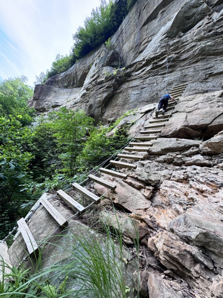 Girl climbing wooden ladder on red over gorge via ferrata