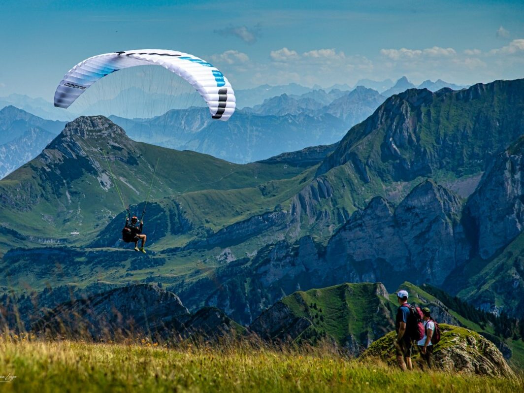 Two people are paragliding over a mountain range